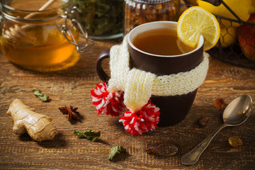 Cozy hot mug of tea wrapped in scarf on wooden table