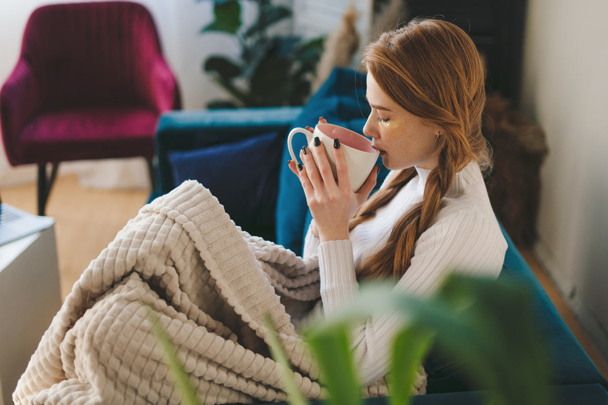 Woman relaxing under a cozy blanket sipping a warm cup of caffeine-free tea